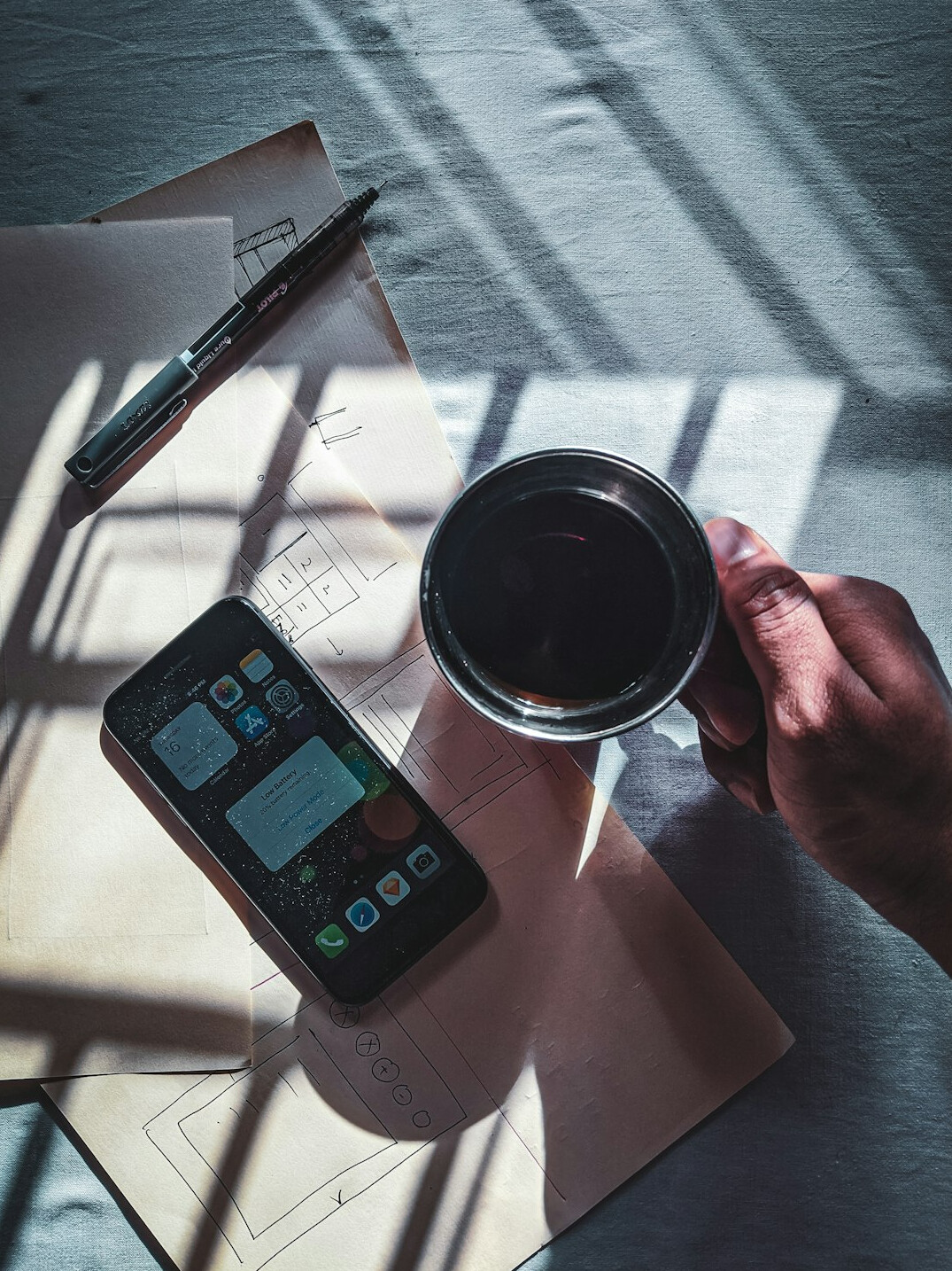 Close-up of hands writing notes in a notebook next to a cup of coffee